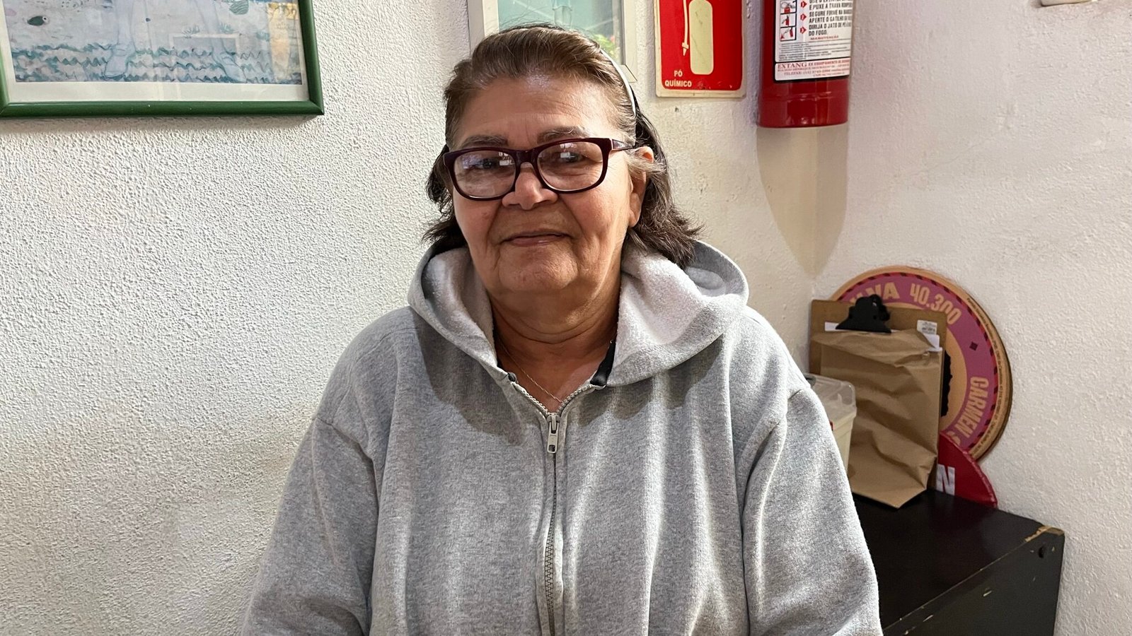Irene da Silva usa óculos, moletom com capuz cinza e sorri para a foto